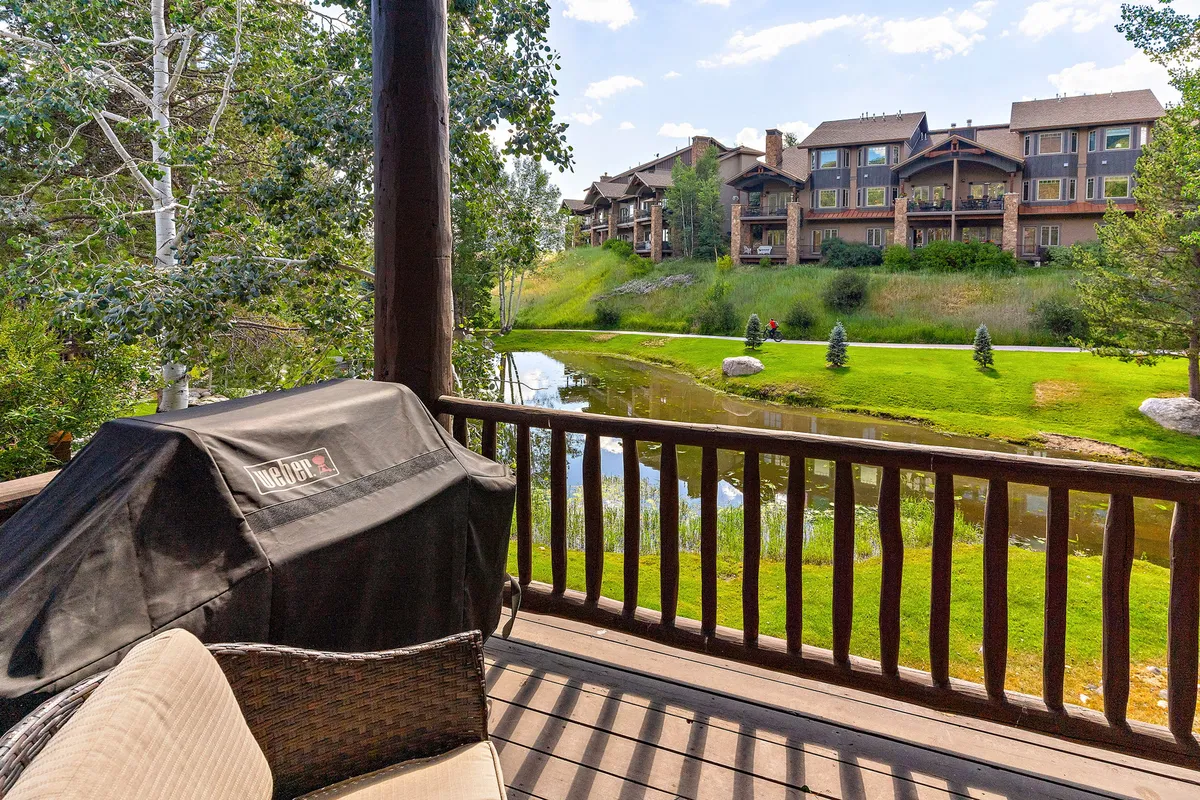 A tranquil creekside patio setting featuring grill, comfortable patio furniture, views of a pond, abundant greenery, and the building facade in the backdrop. The area is ideal for outdoor dining, socializing, or simply soaking up the peaceful creekside ambiance.