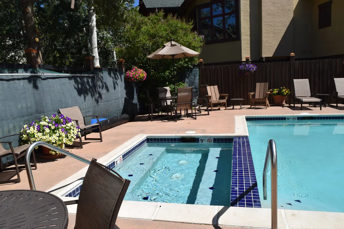 This image captures the inviting outdoor swimming pool and hot tub area, surrounded by comfy lounge chairs, decorative flowers, and an umbrella. The setting looks perfect for both daytime relaxation and evening gatherings, with lush greenery and the resort-style ambiance clearly visible.