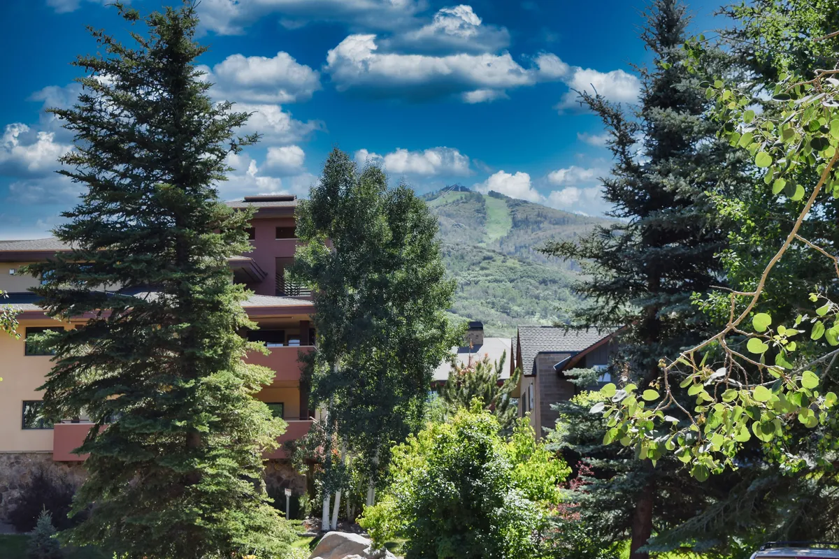This exterior image features a stunning mountain backdrop with lush greenery and the architectural features of the Waterstone buildings in the foreground. The serene landscaping and natural beauty evoke a tranquil, resort-like atmosphere.