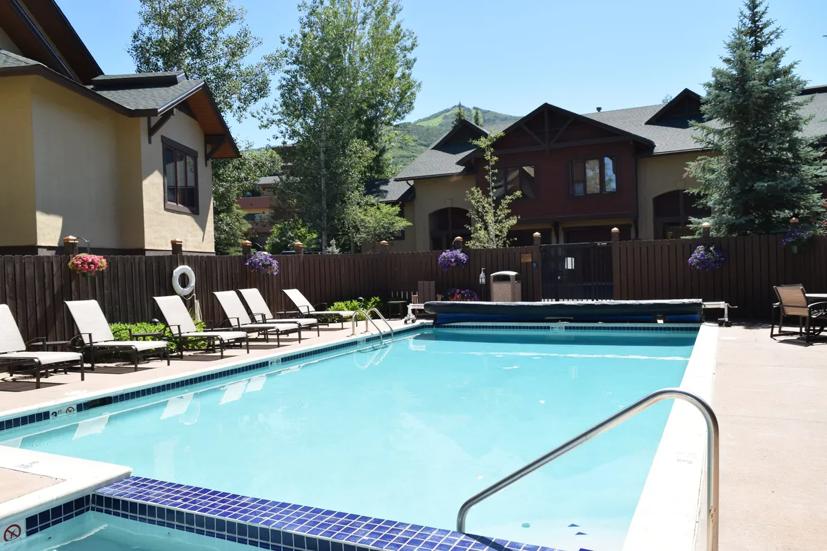 A sparkling outdoor heated pool is surrounded by lounge chairs and mature greenery, adjacent to the Waterstone buildings. The relaxed setup suggests activities like swimming, sunbathing, and unwinding to the sound of the nearby creek.
