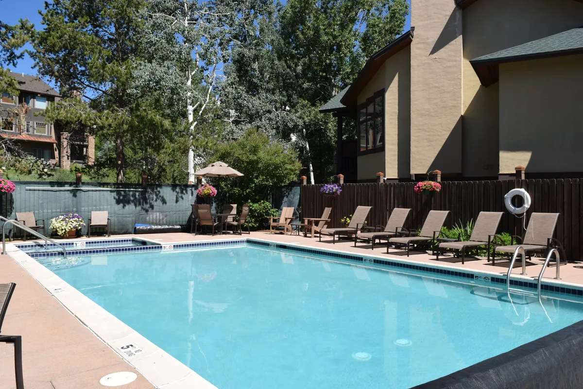 A vibrant outdoor swimming pool surrounded by lounge chairs and lush greenery, with colorful flowers in planters creating a welcoming, leisurely atmosphere. The tranquil setting encourages relaxation, swimming, and socializing, and hints at the community amenities available to guests.