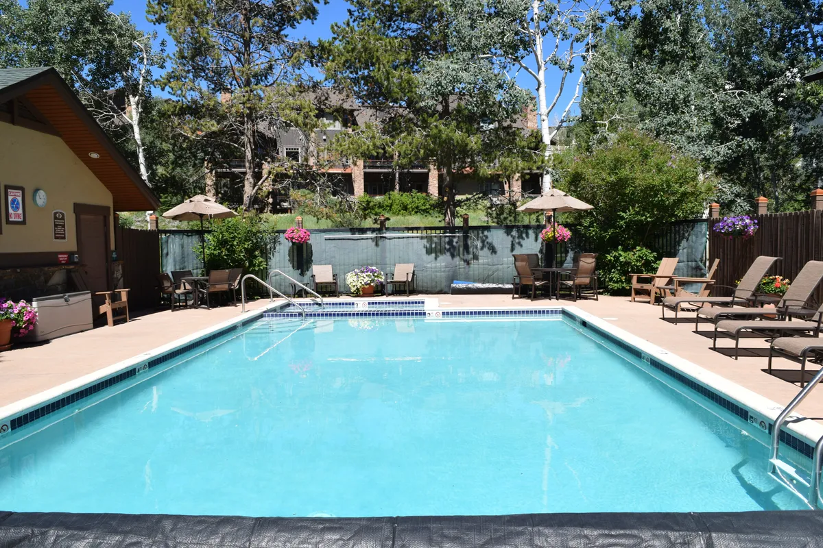 The inviting outdoor heated pool and hot tub, surrounded by lounge chairs and shaded by umbrellas, offers a relaxing space to unwind after an active day. The pool area is clean and well-maintained, set against a scenic backdrop.