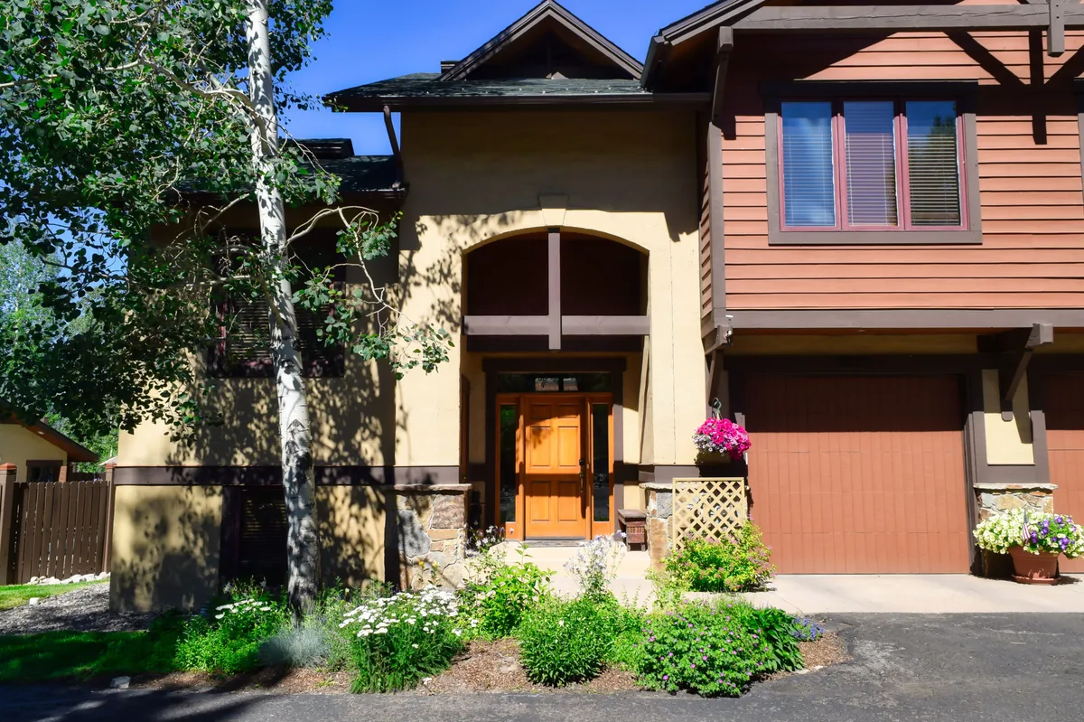 The inviting front entrance of the townhome, framed by flower beds and an aspen tree, with a welcoming porch area perfect for casual outdoor gatherings or enjoying the fresh air with loved ones.
