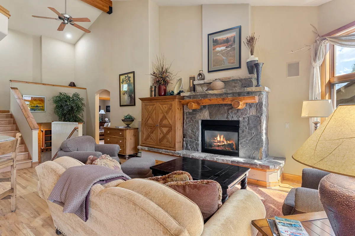 This interior image centers on a welcoming living room featuring a fireplace, a comfortable sofa, wooden furniture, and art on the walls. Sunlight streams in, creating a cozy and inviting atmosphere ideal for gatherings and relaxation after mountain adventures.