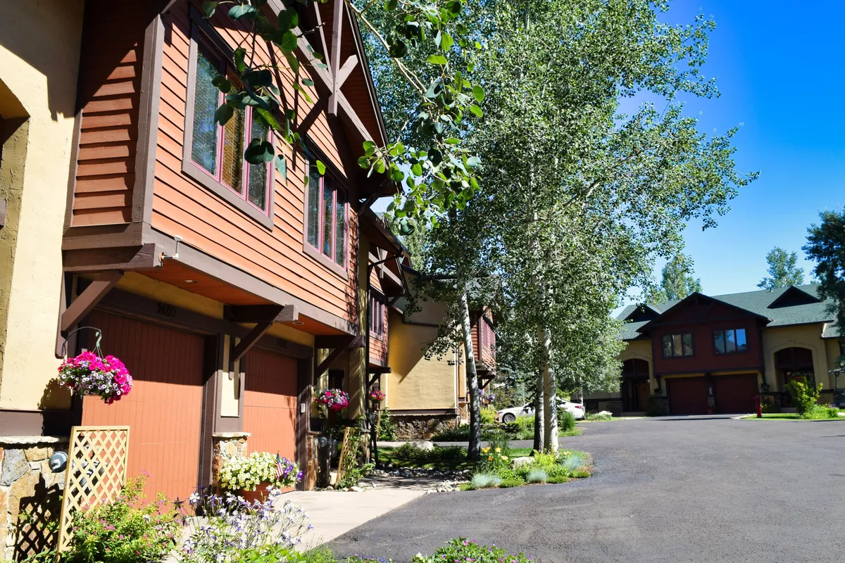 The exterior of the community with flower pots, aspen trees, and charming architectural details. The scene evokes an inviting, serene neighborhood ambiance, ideal for family celebrations, barbecues, and quiet moments outdoors.