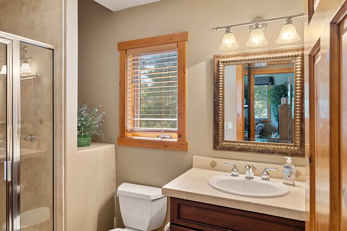 A calm, modern bathroom with a vanity sink, large framed mirror, shower enclosure, and a window with natural light streaming in. The design is clean and accessible, perfect for guest comfort and convenience.